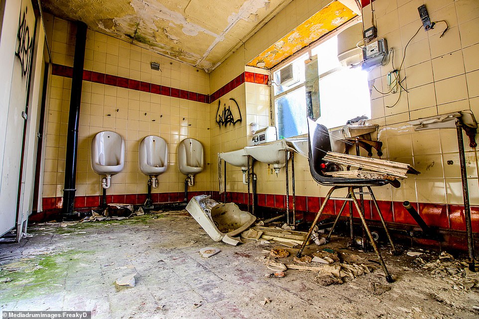 The old bathrooms have been vandalised following the closure 13 years ago which shows a broken sink and urinals with a crumbling ceiling