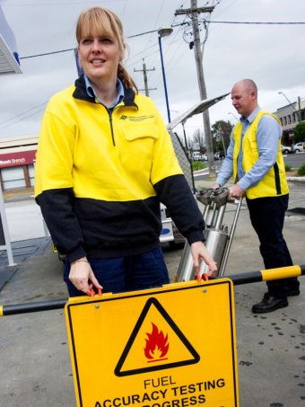 Two inspectors in yellow vests operate equipment at a petrol station