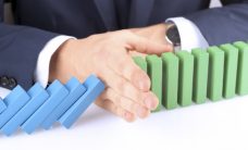 Close-up Of Businessman Stopping The Effect Of Domino With Hand At Desk