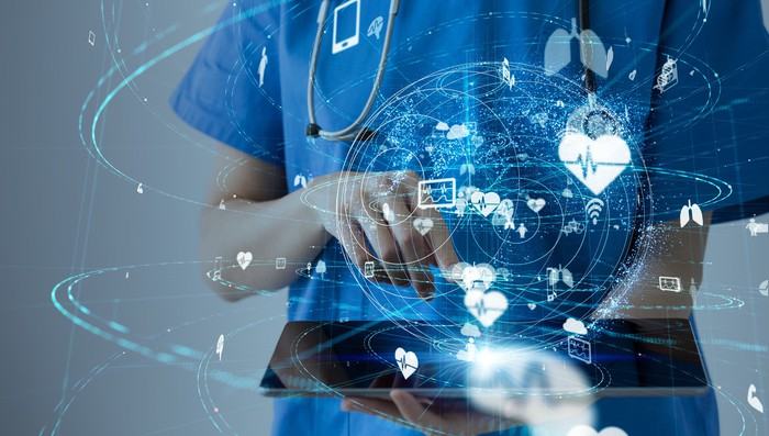 Healthcare professional holding a tablet with healthcare-related images appearing over the tablet.