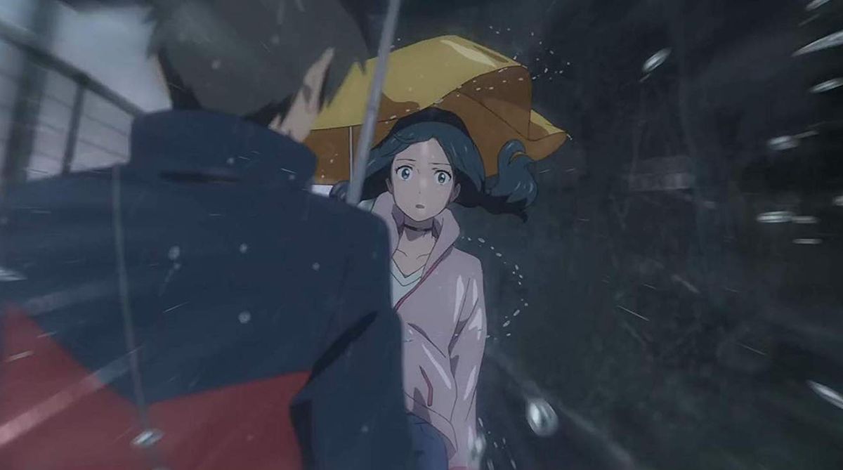 In an image of the anime movie Weathering With You, the camera is approaching through a rainy city towards the protagonist Hina, a young woman with a battered yellow umbrella, who looks surprised while the water swirls around her.