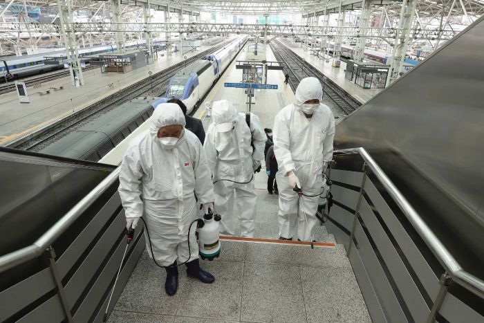 Three men in white protective suits and face masks spray downwards as they walk up stars.