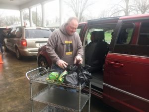 Bill Conger loads bags of food into vehicle parked in the drive through pickup line for the student food distribution Monday