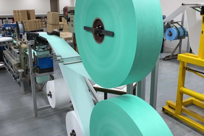 Manufacturing medical masks at Med-con Blue-green material runs through a machine to make medical masks