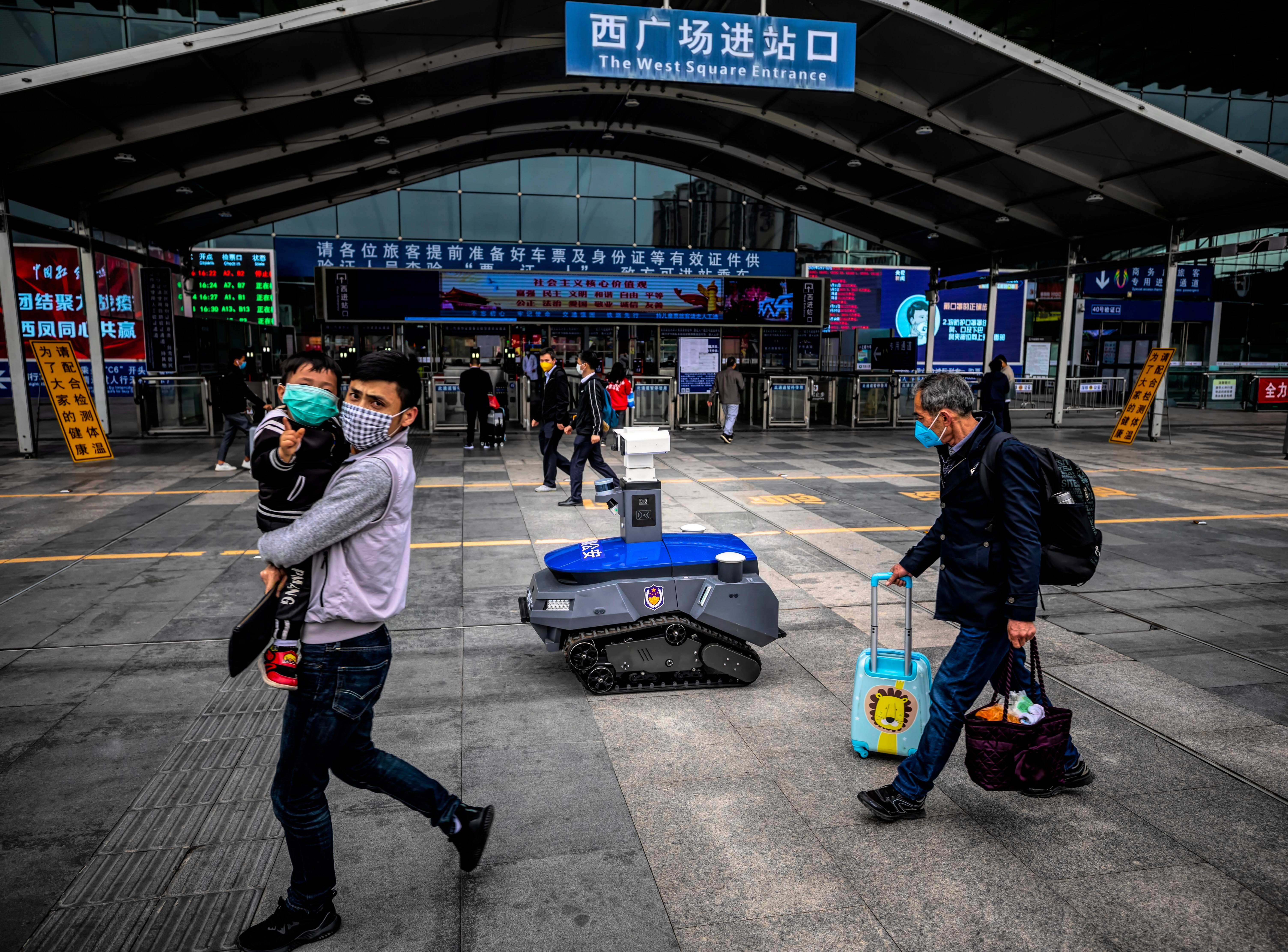 A security robot which warns people when they are not wearing masks and checks their body temperature drives among people on the high-speed railway station platform in Shenzhen