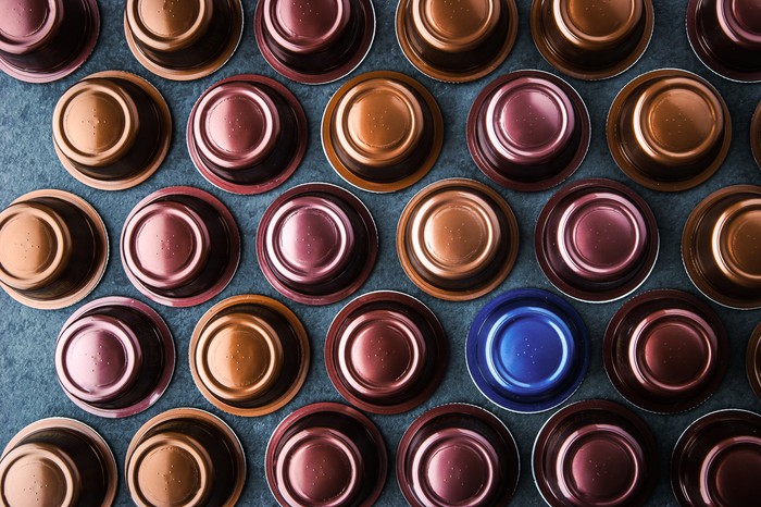 Numerous coffee pods are placed upside down on a blue table top surface.