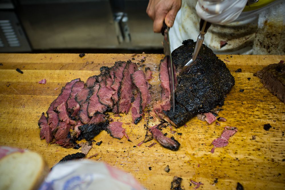 A butcher chops up pastrami on a wooden block at Katz’s