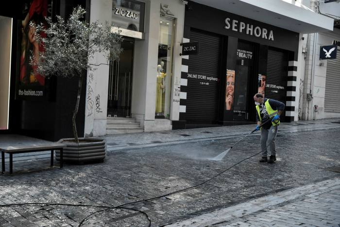 A street cleaner works in front of shuttered clothes shops in Athens. At a time when retailers would normally be placing orders for their Spring 2021 collections, they are instead trying to unpick contracts