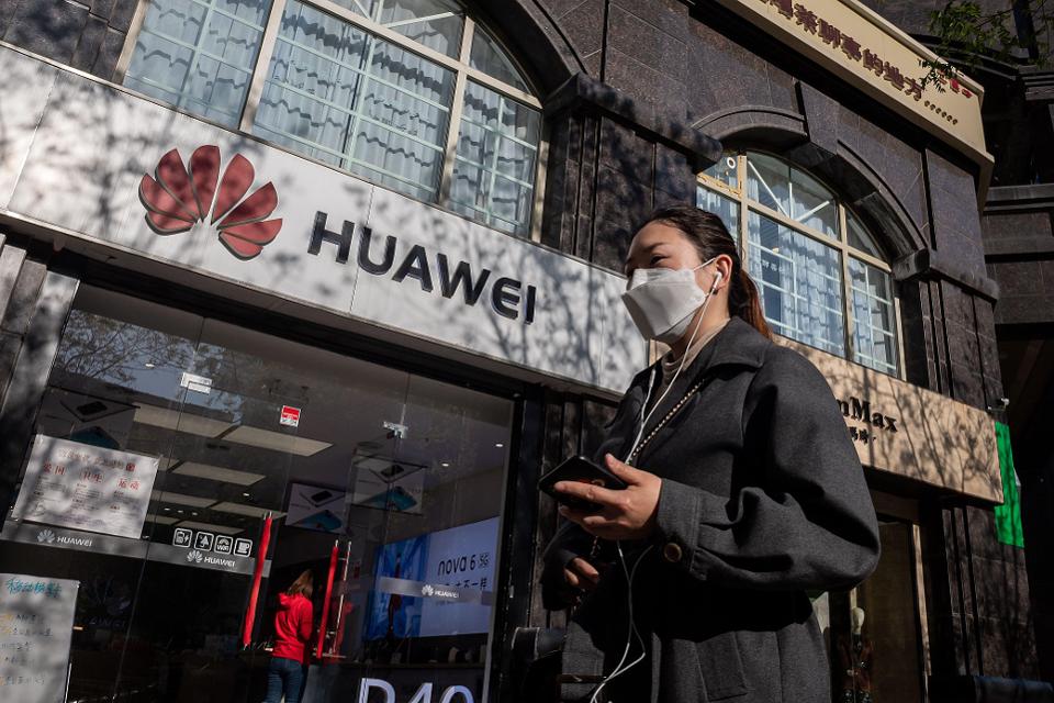 A woman with a smartphone walks past a Huawei shop.