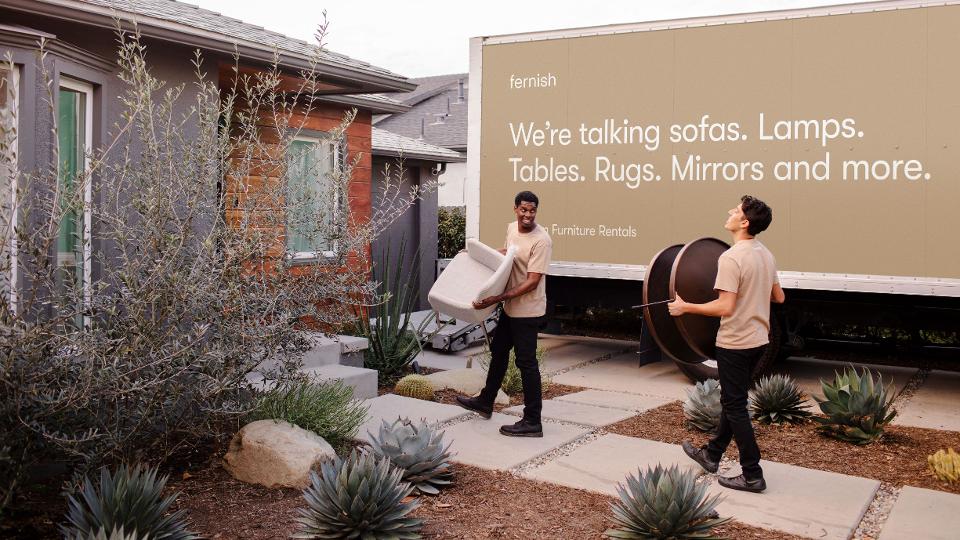 Employees of the furniture rental service Fernish delivering a table and chairs to a home with a Fernish truck in the background.