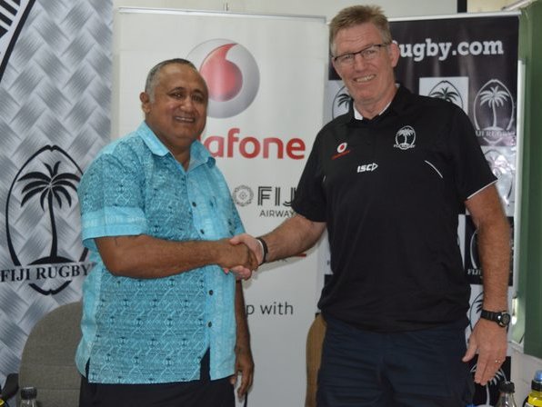 Francis Kean shakes hand with John McKeen against a Fiji Rugby and rugby.com banner