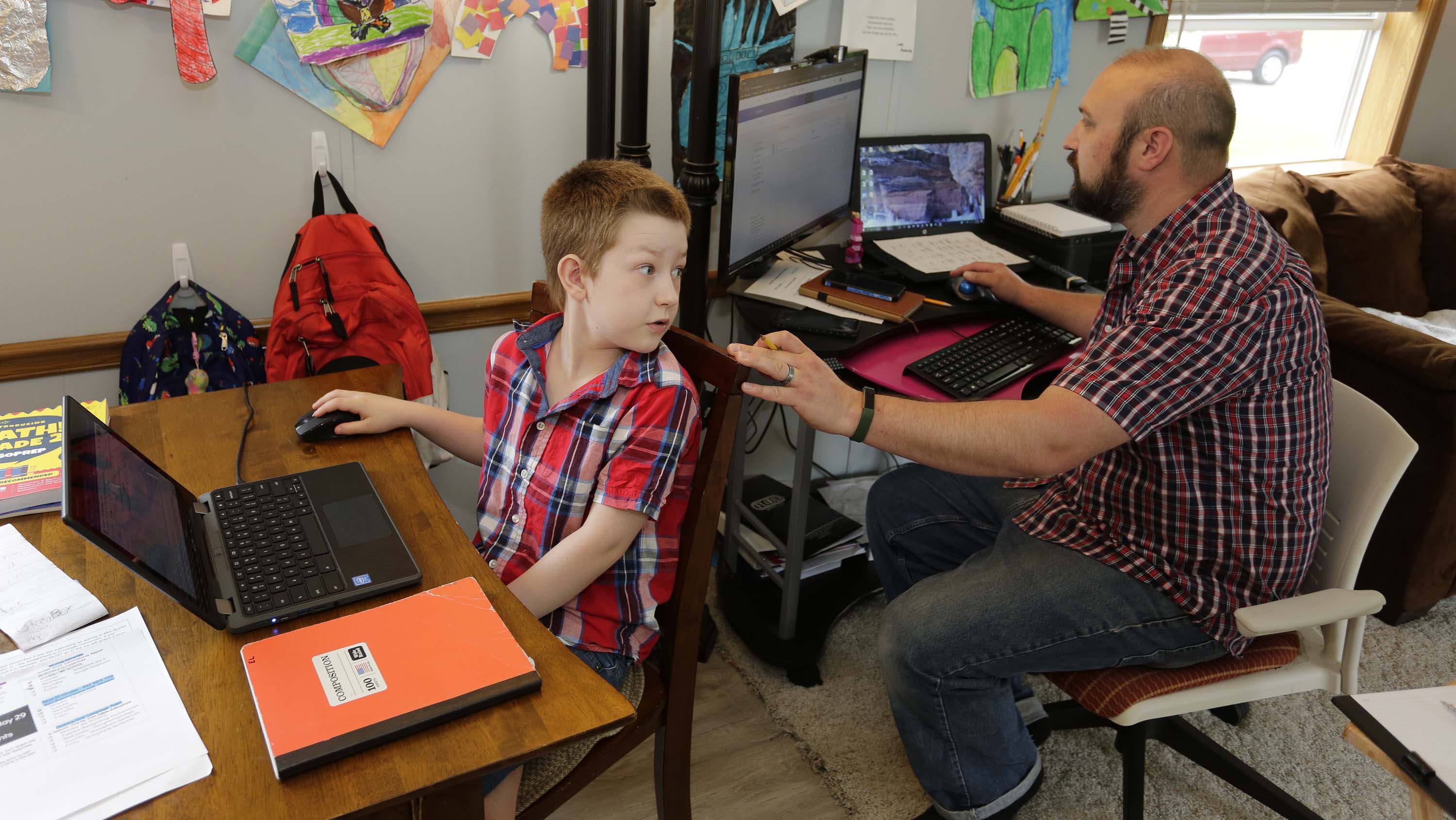 Eli Bartell, 8, turns around to ask his dad, Andy, a question while working on his studies at home last week in Sheboygan.