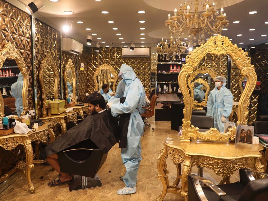 A hairdresser in personal protective suit attends to a customer at a hair salon in New Delhi, India.