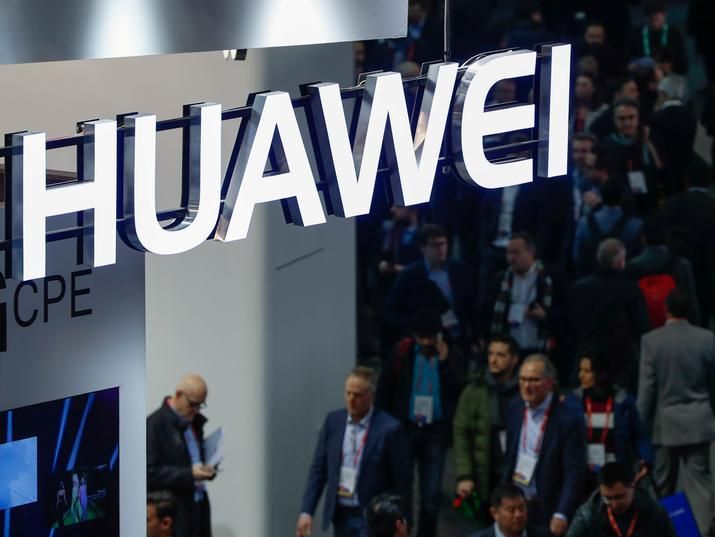 A neon logo of Huawei suspended above a passing crowd