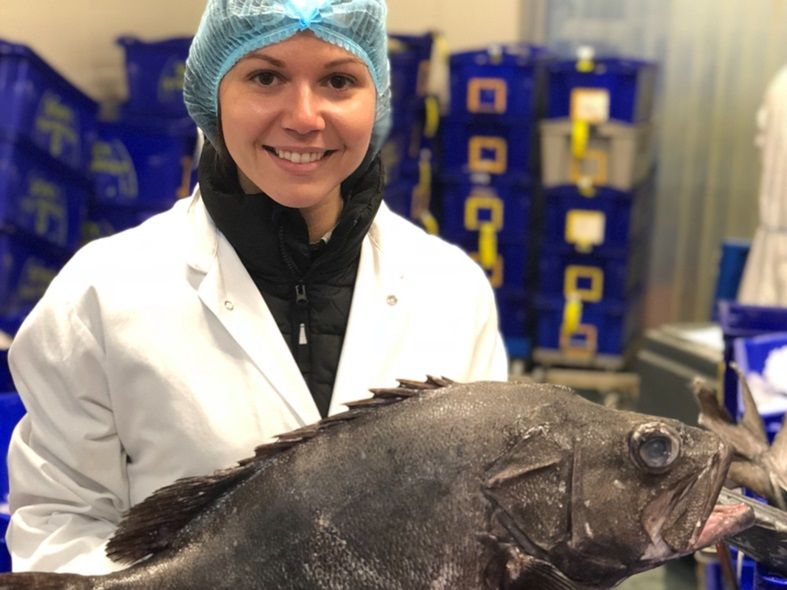 A woman with a protective cap on is holding a large fish.