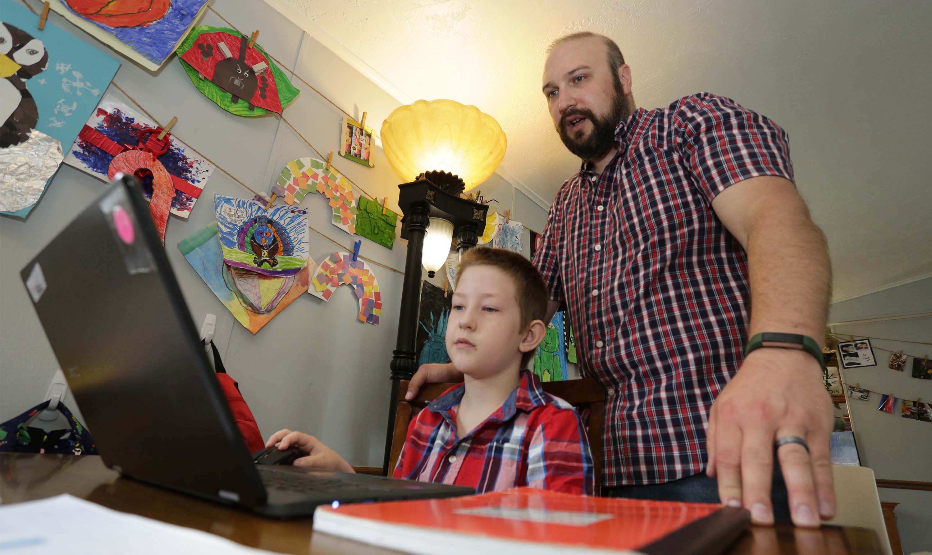 Eli Bartell, 8, left, works on homework at the kitchen table as his dad Andrew gives him guidance last week in Sheboygan.