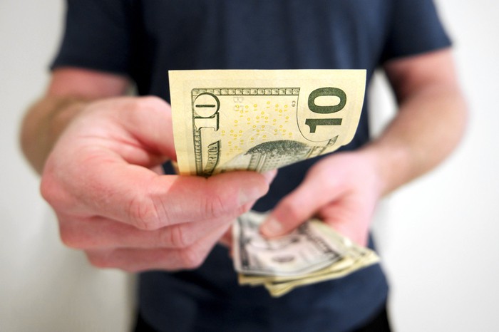 Man's hand offering a $10 bill from his stack of paper money