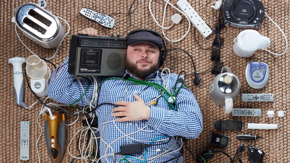 Ian Downs, a.k.a. DJ Downsy, surrounded by old hoarded electrical appliances. 