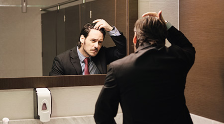 Man fixing his hair in front of restroom mirror