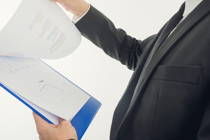 A man in a suit looking over paperwork on a clipboard
