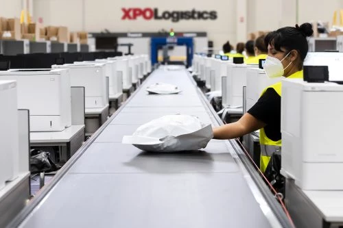 XPO warehouse workers wearing PPE and placing packages on a conveyer belt