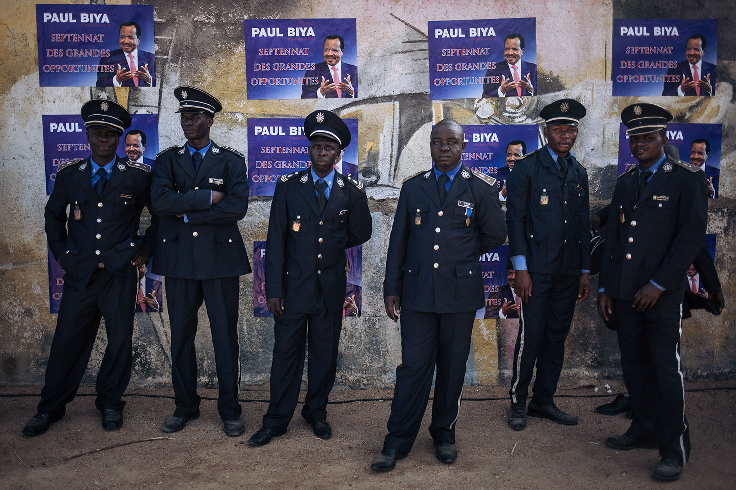 Policemen wait in the shade after the electoral meeting in front of posters for President Paul Biya in Maroua on Sept. 29, 2018.