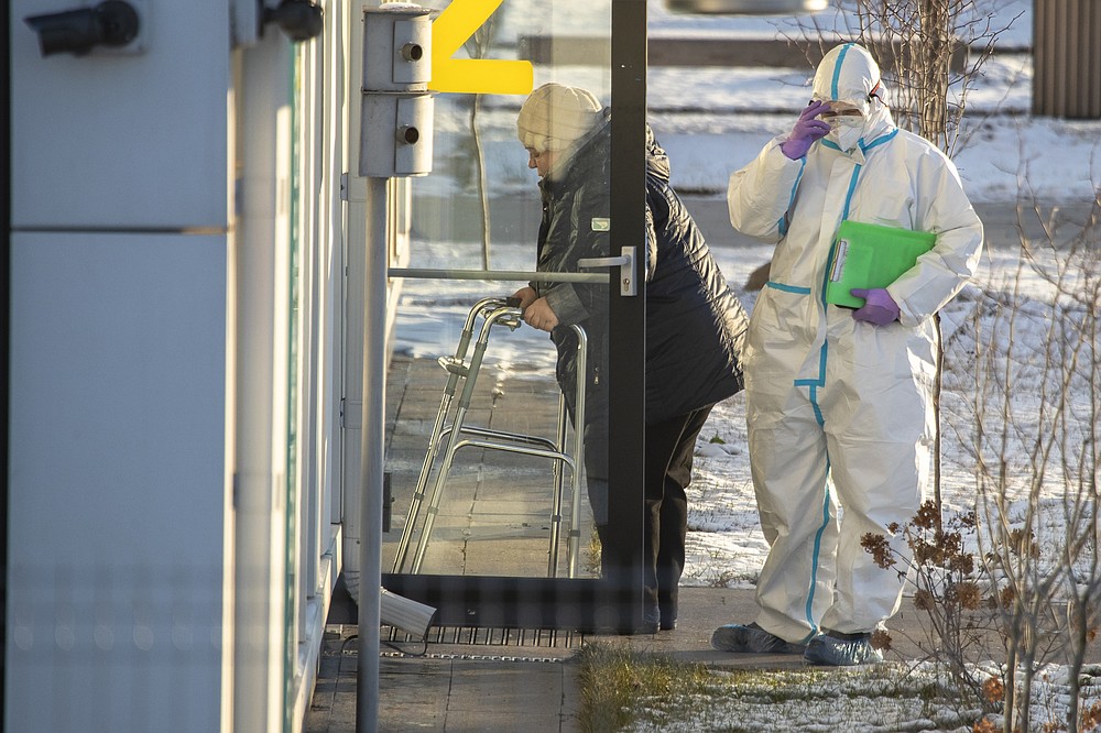 A medical worker wearing protective gear escorts a woman, suspected of having coronavirus, at a hospital in Kommunarka, outside Moscow, Russia, Saturday, Dec. 5, 2020. Thousands of doctors, teachers and others in high-risk groups have signed up for a COVID-19 vaccination in Moscow starting Saturday, a precursor to a Russia-wide immunization effort. (AP Photo/Pavel Golovkin)