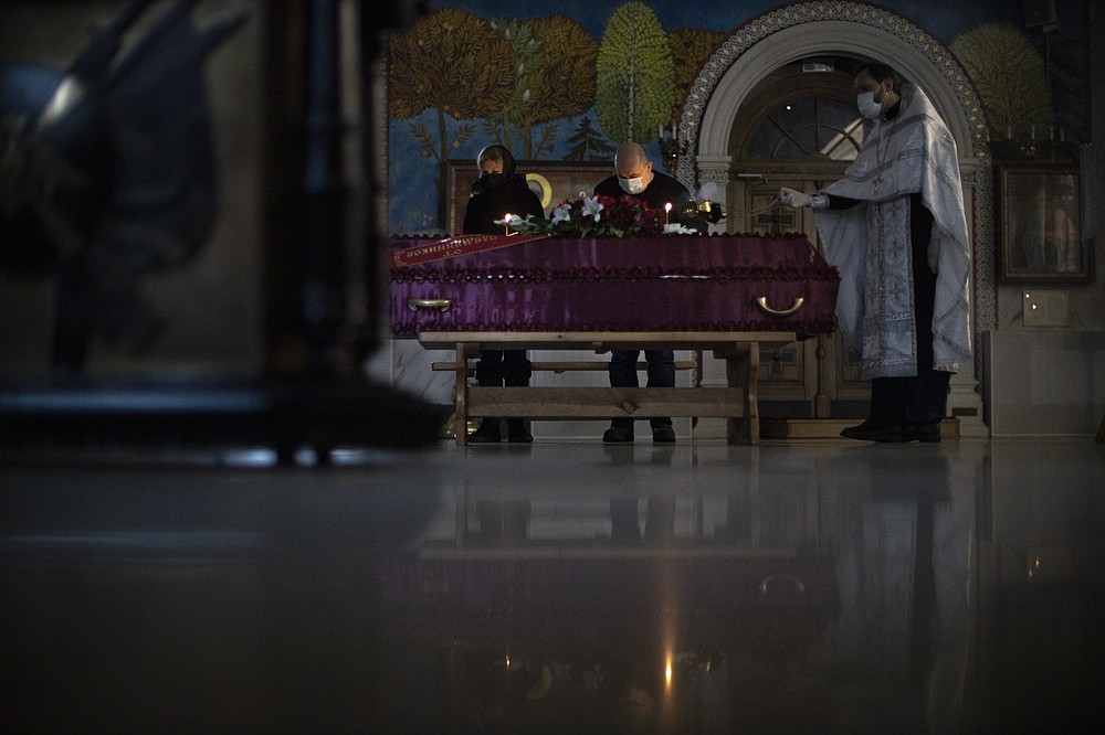 Father Vasily Gelevan, wearing a face mask and gloves to protect against the coronavirus, conducts a funeral service for a person who died of COVID-19 as only two relatives stand next a coffin amid the outbreak at the Church of the Annunciation of the Holy Virgin in Sokolniki in Moscow, Russia, Friday, Dec. 4, 2020. Russia has been swept with a resurgence of the outbreak this fall, with numbers of new infections exceeding the levels recorded early in the pandemic. (AP Photo/Alexander Zemlianichenko)