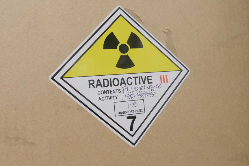A brown cardboard box with a sticker on the front reading 'radioactive contents: Fluorine18'. 