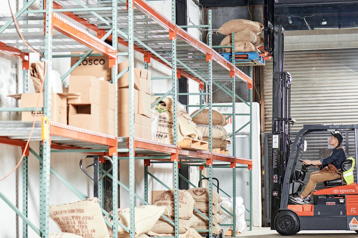 A forklift can be seen trying to lift coffee bags on shelves placed along the wall inside Shared Roasting