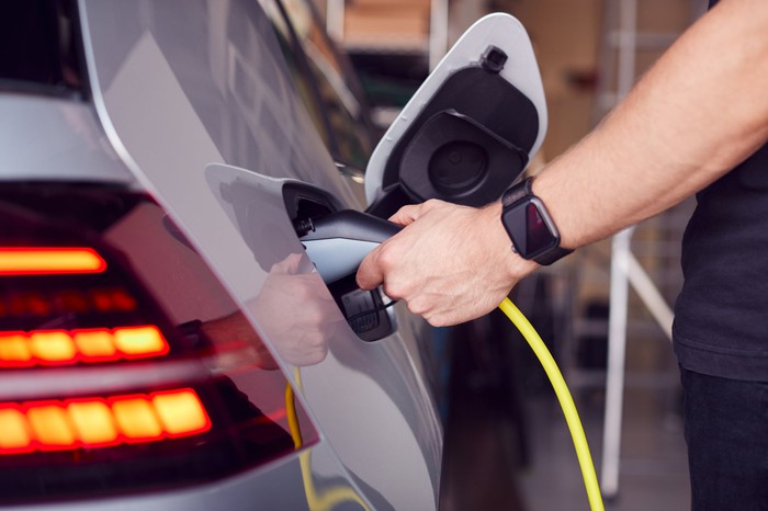 A person's arm attaches a power cable to an electric vehicle.