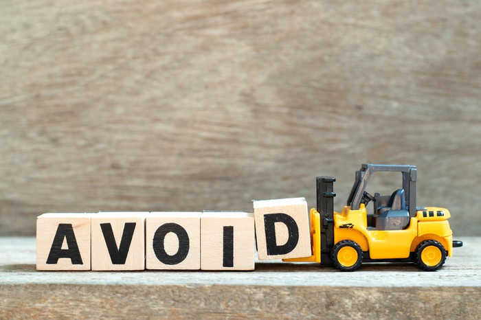 A toy forklift holds the letter block D to complete the word AVOID.