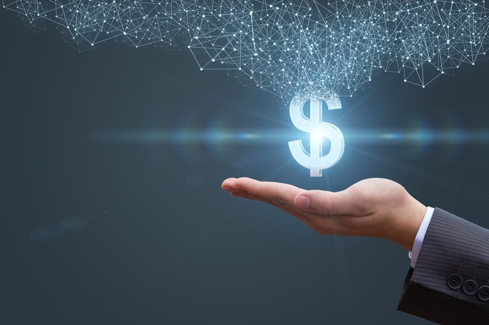 Image of a lighted dollar sign with a grid of connected nodes over a man's outstretched palm