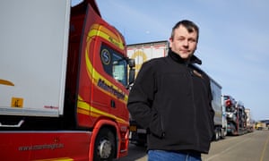 Stephen Connor in a zip-up jacket with his hands in his pockets, standing by his red and yellow lorry