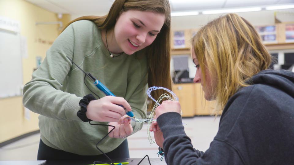 Students work together with a 3D pen in a classroom.