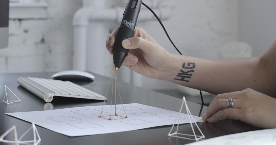 A woman draws a three-dimensional pyramid with a 3D printing pen.
