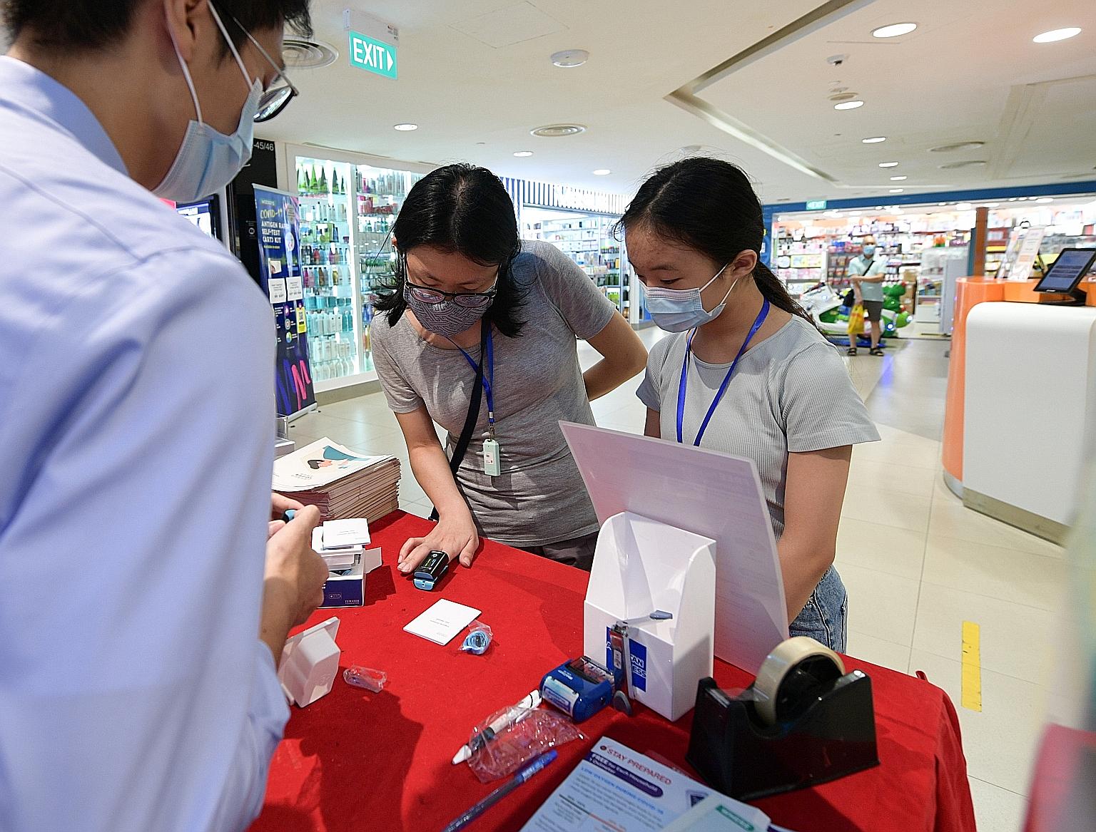 Intern pharmacist Kenji Ng testing an oximeter for Tan Wee Sun, 41, and Isabelle Chiam, 11, at Watsons' Junction 8 outlet. Steady queues formed at multiple pharmacies islandwide yesterday - the first day of the free oximeter distribution - with some 