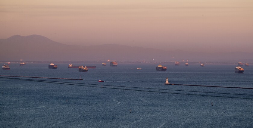 The sunset illuminates dozens of container ships in the ocean off the coast
