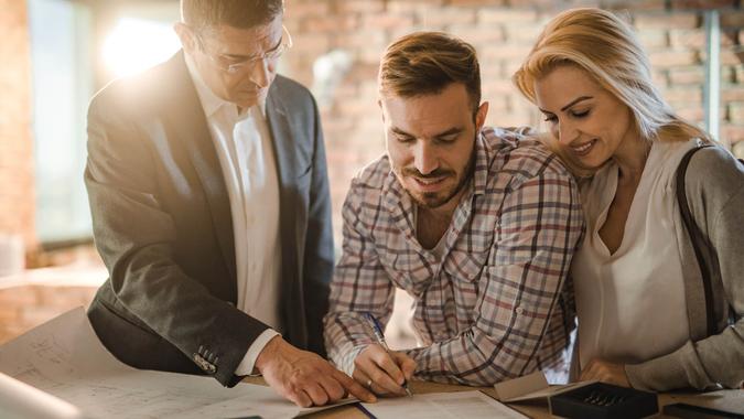 Mid adult investor showing young couple where to sign the contract for buying a house.