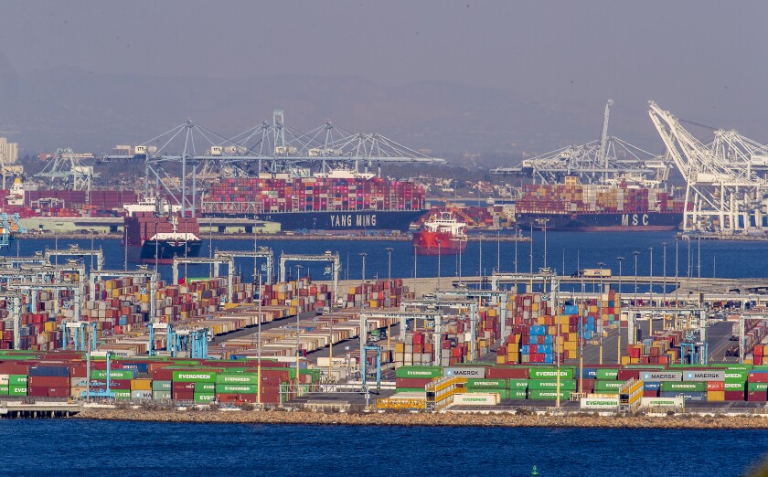 Container ships sit off the coast of the ports of Los Angeles and Long Beach, and many containers sit stacked on land.