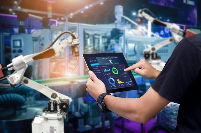 A person using a tablet to operate a robotic arm in a digital factory.
