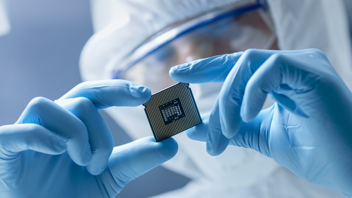 Someone in a lab suit holds a semiconductor.