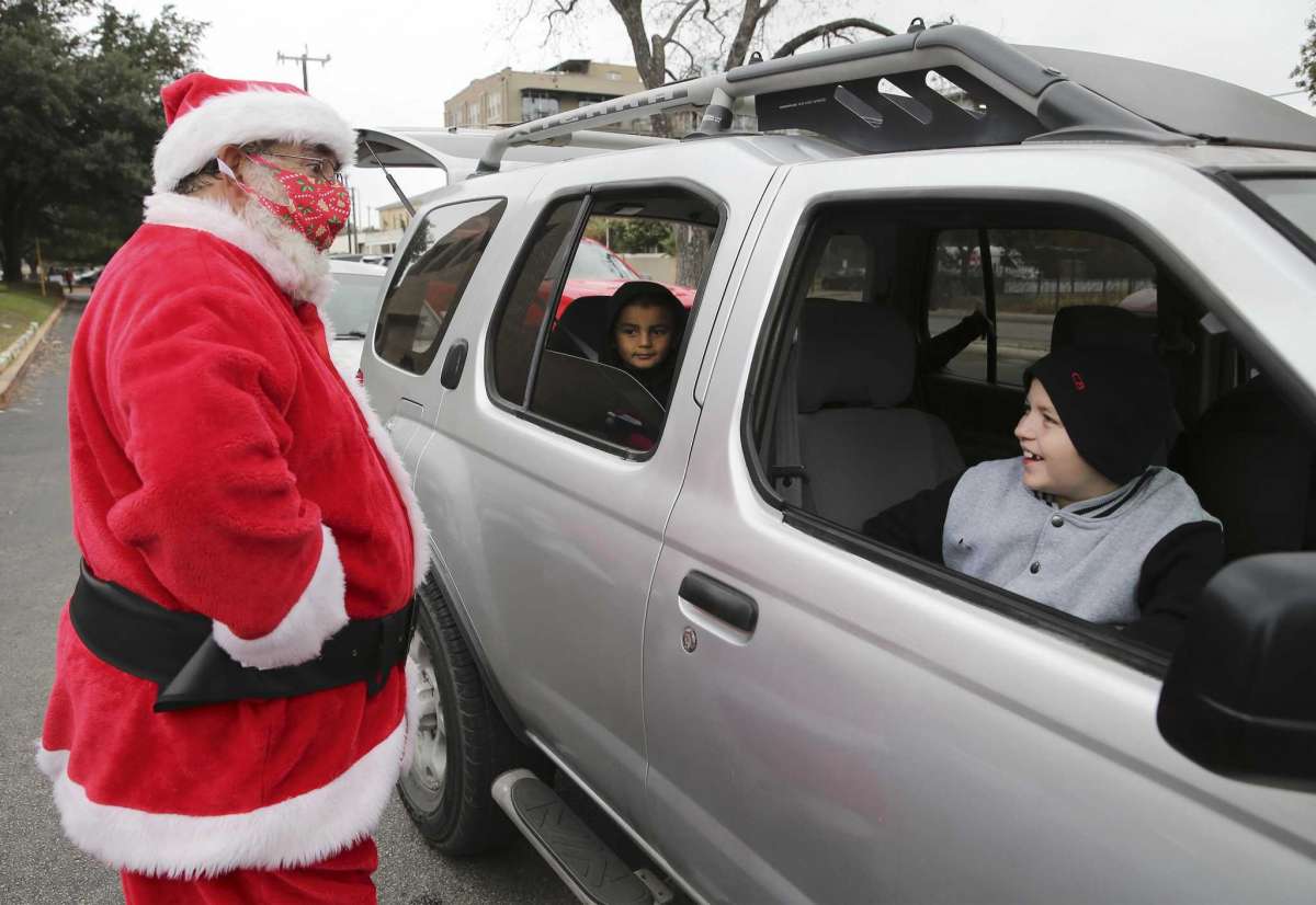 Michael Reyes dresses as Santa as he interacts with Branden (right) and Brenda Perryman (in back seat) during a toy distribution at San Antonio Housing Authority on Wednesday, Dec. 23, 2020.