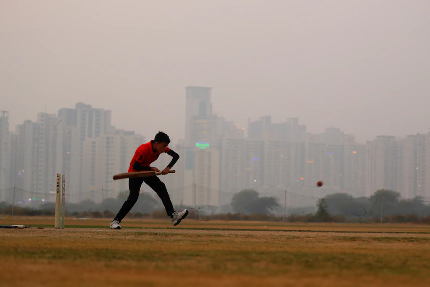 A boy plays cricket amidst smog at a playground.