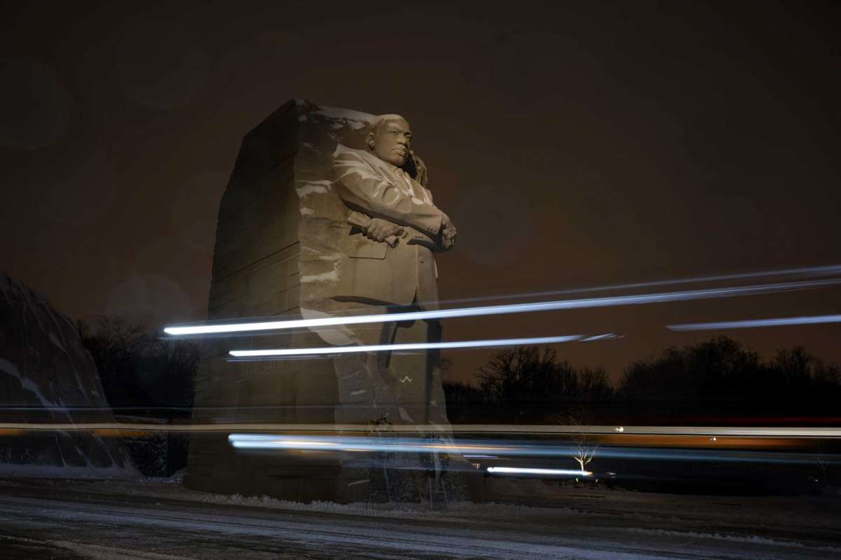 In this photo made with a long exposure, snowplow lights streak past the Martin Luther King Jr. Memorial in Washington, Sunday, Jan. 16, 2022. Ceremonies scheduled for the site on Monday to mark the Martin Luther King Jr. national holiday, were canceled because of the weather.