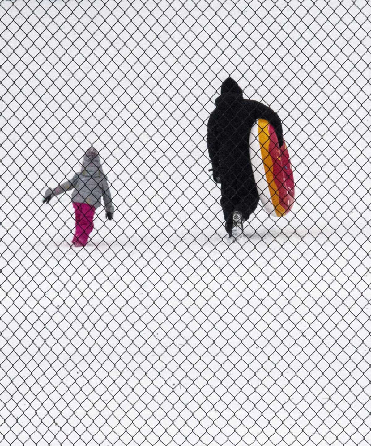 Seen through a basketball court's chain link enclosure, tubers head back up a hill for another run on the fresh snow at Raleigh Court Park on Monday Jan. 17, 2022 in Roanoke, Va.