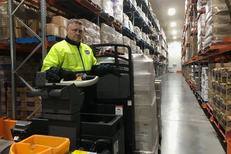 A man in a high-vis vest on a forklift in a large warehouse.