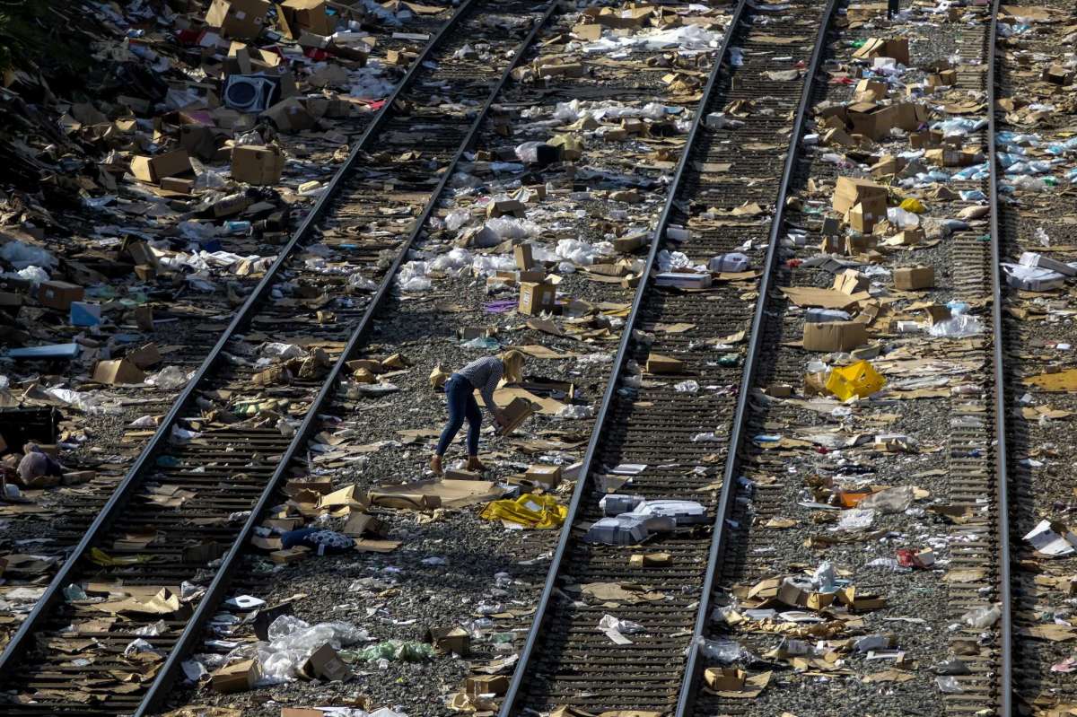 A member of the media picks up a shredded box at a section of the Union Pacific train tracks in downtown Los Angeles, Friday, Jan. 14, 2022. Thieves have been raiding cargo containers aboard trains nearing downtown Los Angeles for months, leaving the tracks blanketed with discarded packages. The sea of debris left behind included items that the thieves apparently didn't think were valuable enough to take, CBSLA reported Thursday, Jan. 13.