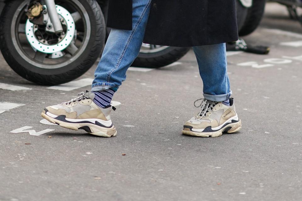 PARIS, FRANCE - JANUARY 20: A guest wears a black long coat, blue denim jeans pants, beige leather sneakers from Balanciaga, outside Rains , during Paris Fashion Week - Menswear F/W 2022-2023, on January 20, 2022 in Paris, France. (Photo by Edward Berthelot/Getty Images)