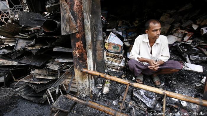 A man sits in front of his burnt-out shop